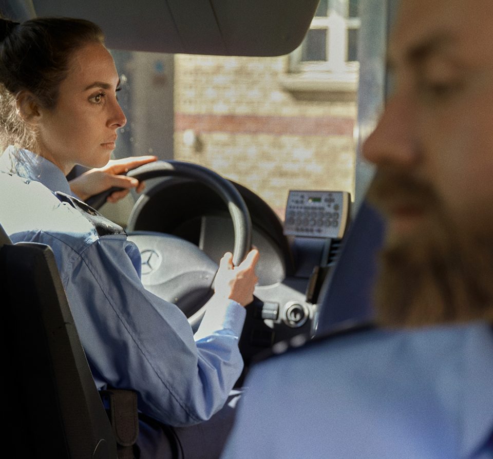 to transportbetjent i en bil. en kvindelige transportbejtent kører. en mandlig transportbetjent sidder bag ved og vender sig mod hende.