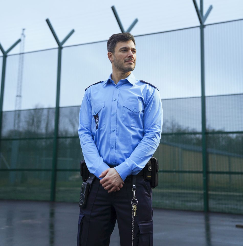 fængselsbetjent mand står foran hegn udendørts